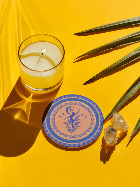Round ceramic coaster featuring a silhouetted dancing figure reaching toward a crescent moon, surrounded by concentric rings of stars and floral patterns in blue on peach background
